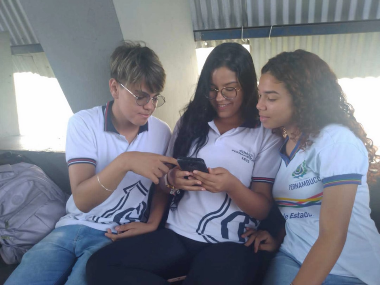 three girls sitting on a couch looking at a cell phone — Foto por cham5 champoleiro na Unsplash