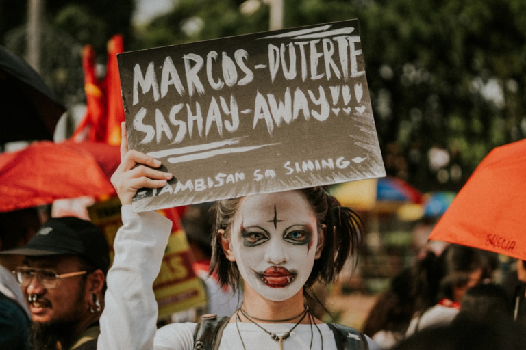 Person with clown makeup holds protest sign — Foto por Joaquin Arenas na Unsplash
