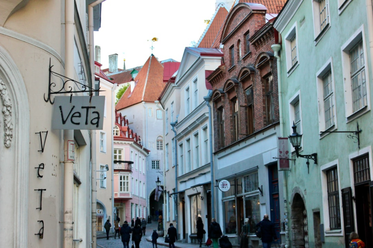 a group of people walking down a street next to tall buildings — Foto por 66 north na Unsplash